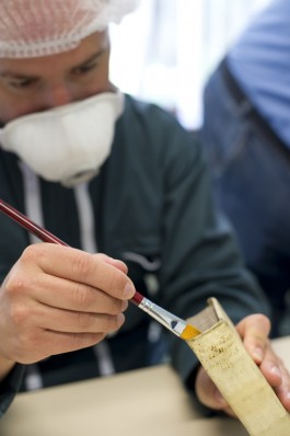 Man met mondmasker veegt met een borstel stof van de bovensnede van een boek