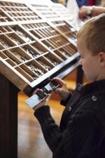 Jongen met zethaak aan de letterbak | Foto: Sven Van Baarle Jongen met zethaak aan de letterbak
