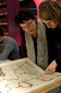 Twee vrouwen buigen zicht over een historische atlas