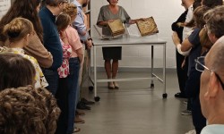 Een groep mensen bekijken een presentatie van twee boeken door een vrouw